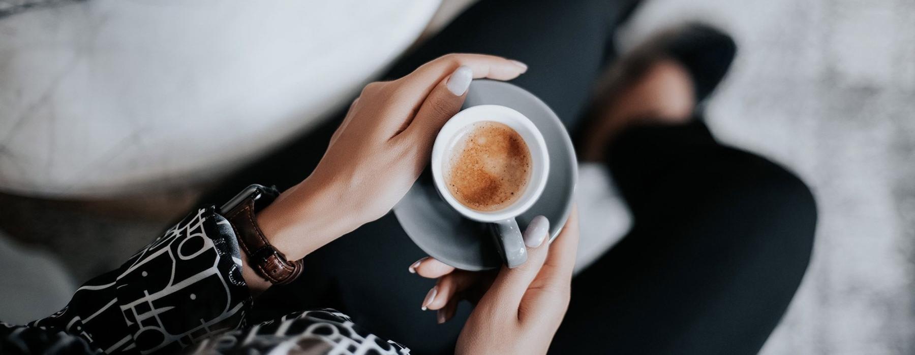 business woman sits next to a marble table with books and holds a saucer with a cup of espresso